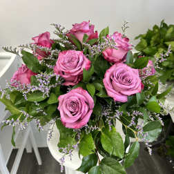Hand-tied bouquet of bright pink roses with small purple filler flowers in a rounded design