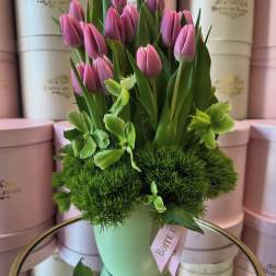 Pink tulips arranged in a pale green vase with green blooms