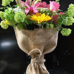 Bouquet of pink lilies and yellow sunflowers wrapped in burlap