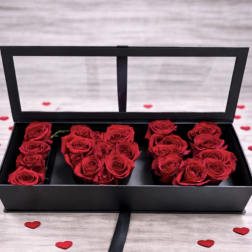 Red roses arranged in a black rectangular box with clear lid, surrounded by small red heart accents