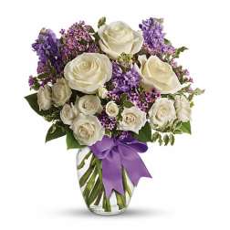 White roses and purple flowers in a glass vase with a purple ribbon