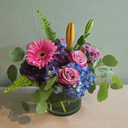 Pink gerbera, roses, blue hydrangea, and lilies in a glass vase