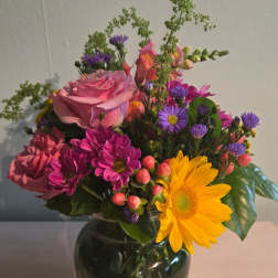 Mixed bouquet of pink roses, purple daisies, and a yellow gerbera in a glass vase