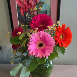 Bright pink and orange gerbera daisies with small white daisies in a clear glass vase.