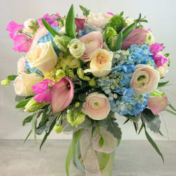 Bouquet of pastel roses, ranunculus, hydrangeas, and calla lilies in a glass vase