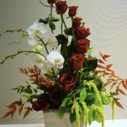Tall arrangement of red roses and white orchids in a white vase