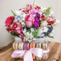 Mixed pink and white flower bouquet above a box of macarons with a pink ribbon