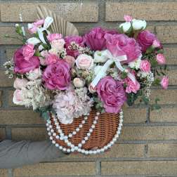 Pink rose bouquet in a wicker basket with white ribbon and pearl strands