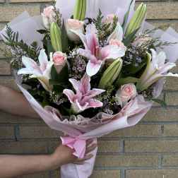 Pink roses and lilies in a wrapped bouquet with a satin ribbon