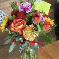 Mixed bouquet of roses, tulips, carnations, and chrysanthemums in a glass vase