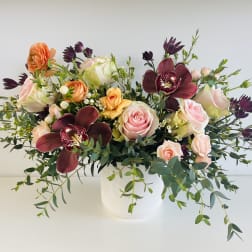 Mixed bouquet of pink and peach roses with dark orchids in a white vase