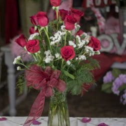 Red roses arranged in a clear glass vase with a red ribbon