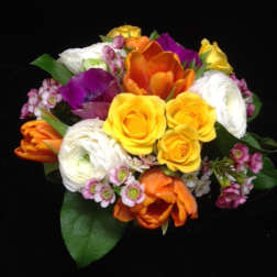 Compact bouquet of yellow roses, orange tulips, white blooms, and purple accents on a black background