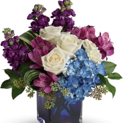 Bouquet of white roses, purple flowers, and blue hydrangea in a square vase