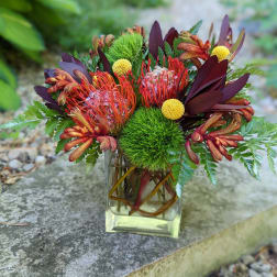 Tropical bouquet in a clear glass vase with orange and burgundy blooms