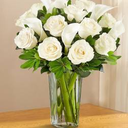 White roses and calla lilies arranged in a clear glass vase