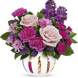 Pink and purple flower arrangement in a white vase with striped candle designs