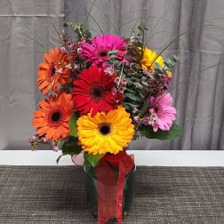 Colorful gerbera daisy bouquet in a glass vase with a red ribbon