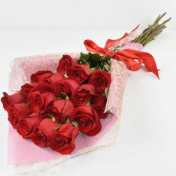 Hand-tied bouquet of long-stem red roses wrapped in pink lace paper with a red ribbon bow
