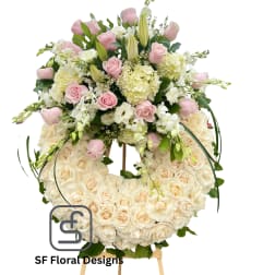 Large ivory rose wreath with pink roses, lilies, and white blooms arranged on top, displayed on a wooden easel.