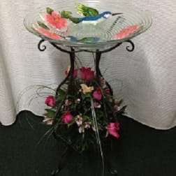 Glass birdbath with pink flowers and a floral base arrangement