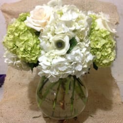 White and green floral arrangement in a round glass vase
