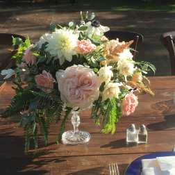 Pastel floral centerpiece in a clear pedestal vase on a wooden table