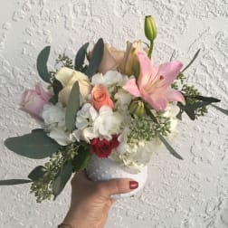 Handheld bouquet of pink lilies, roses, and white hydrangeas in a white vase
