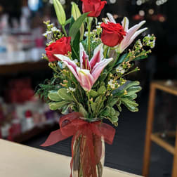 Red roses and pink lilies in a clear glass vase with a red ribbon