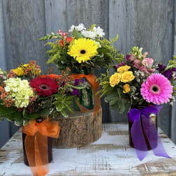 Three colorful flower arrangements in ribbon-tied vases on a rustic table