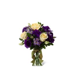 Small vase arrangement of cream roses, purple lisianthus, and lavender asters in a ribboned glass vase.
