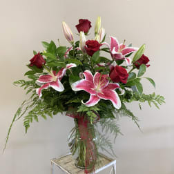 Tall vase arrangement of red roses and pink lilies with a red ribbon bow.