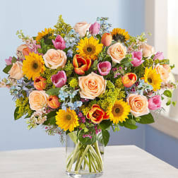 Mixed bouquet of roses, tulips, and sunflowers in a clear glass vase
