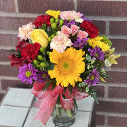 Mixed bouquet with sunflowers, roses, carnations, and daisies in a glass vase