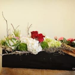 Low floral arrangement with red roses, white hydrangeas, and pink blooms in a black container