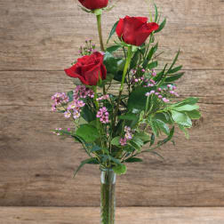 Three red roses in a clear glass vase with pink filler flowers