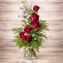 Red roses in a clear glass vase with mixed greenery and small purple flowers