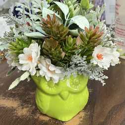 Artificial flowers arranged in a bright green owl-shaped planter