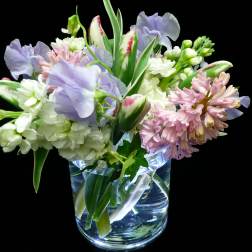 Small vase arrangement of pastel tulips, stock, hyacinth, and sweet peas on a black background