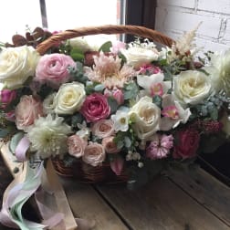 Basket arrangement of pink and white roses with mixed blooms and ribbon
