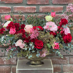 Low floral arrangement of red and pink roses in a gold vase