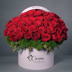 Red roses arranged in a round pink hat box with green filler at the base