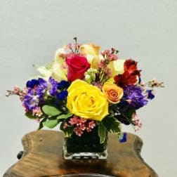 Colorful bouquet of roses and mixed flowers in a square glass vase