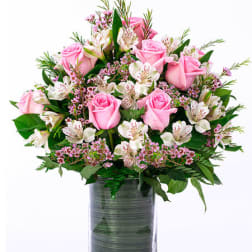 Pink roses and white alstroemeria arranged in a leaf-lined clear glass vase