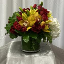 Red roses and yellow orchids in a glass vase with white hydrangea