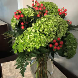 Green hydrangea bouquet with red berry stems in a glass vase