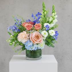 Mixed bouquet of roses, blue flowers, and white daisies in a glass vase
