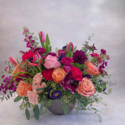 Mixed pink, peach, and purple flowers arranged in a gray bowl