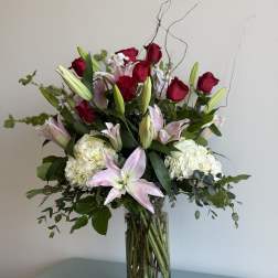 Tall bouquet of red roses, pink lilies, and white hydrangeas in a glass vase