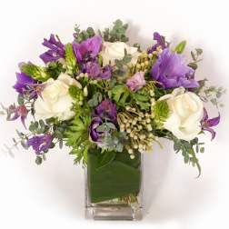 Purple and white flower bouquet in a clear square vase